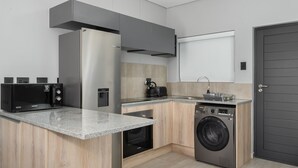 A compact kitchen with a built-in microwave, oven, and washing machine. - Light and Cozy Blouberg Apartment (Cape Town)