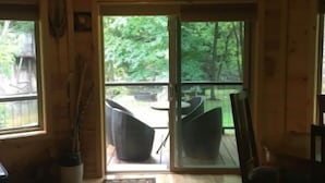 A wooden cabin interior with a sliding glass door leading to an outdoor patio with wicker furniture. - Riverfront! Private, short walk to town (Hot Springs)