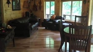 A wooden cabin interior with a living room, dining area, and large windows. - Riverfront! Private, short walk to town (Hot Springs)