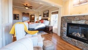 A spacious bedroom with a large bed, a stone fireplace, and a ceiling fan.