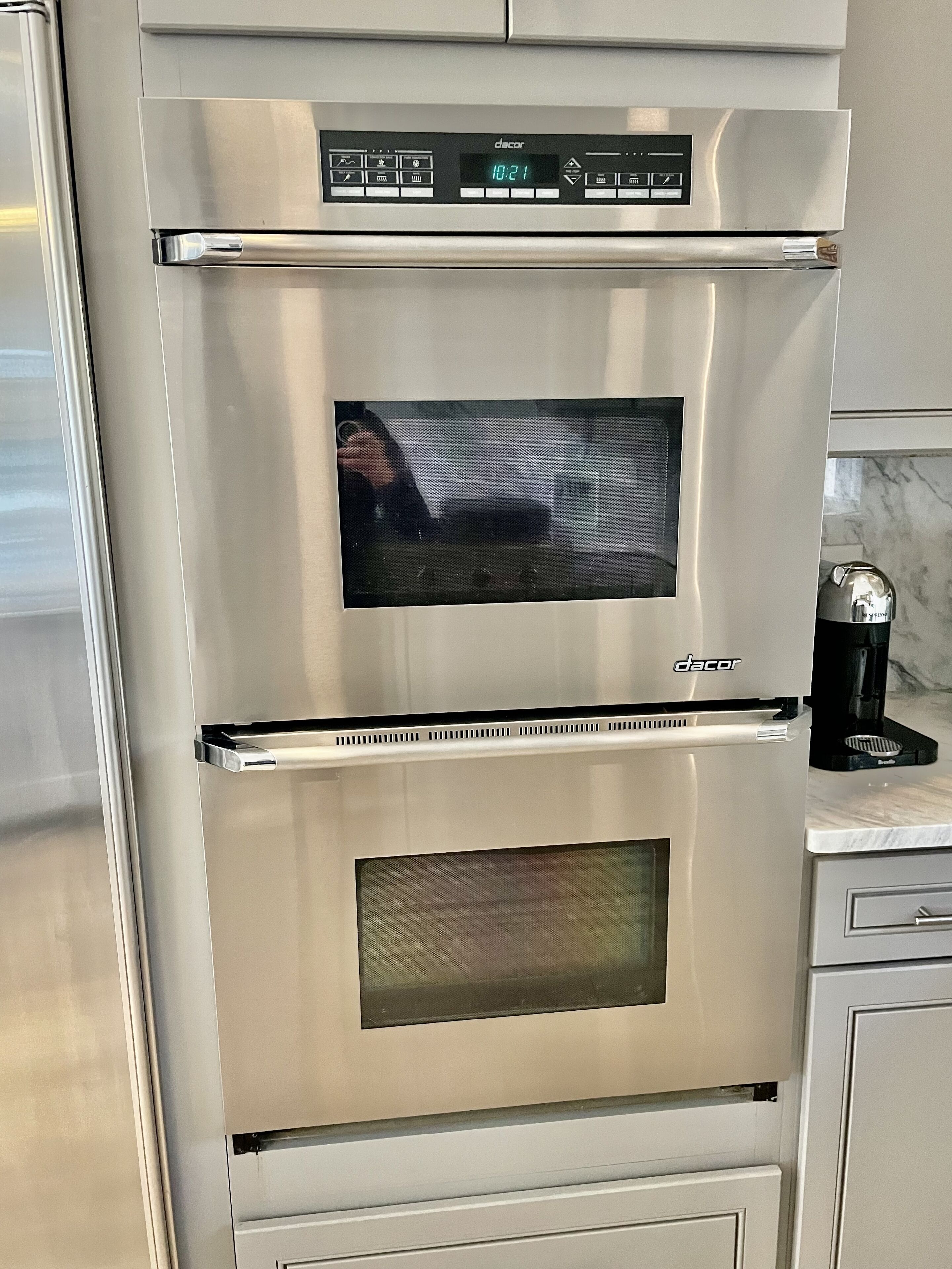 A stainless steel Dacor oven with a digital clock display, a microwave, and a coffee maker on the countertop.