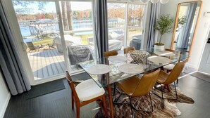 Un espace repas moderne avec une table en verre, des chaises en cuir et une vue sur un lac et une jetée.