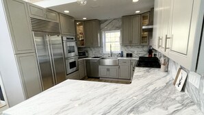 Une cuisine moderne dotée de plans de travail en marbre, d’appareils électroménagers en acier inoxydable et de luminaires suspendus.