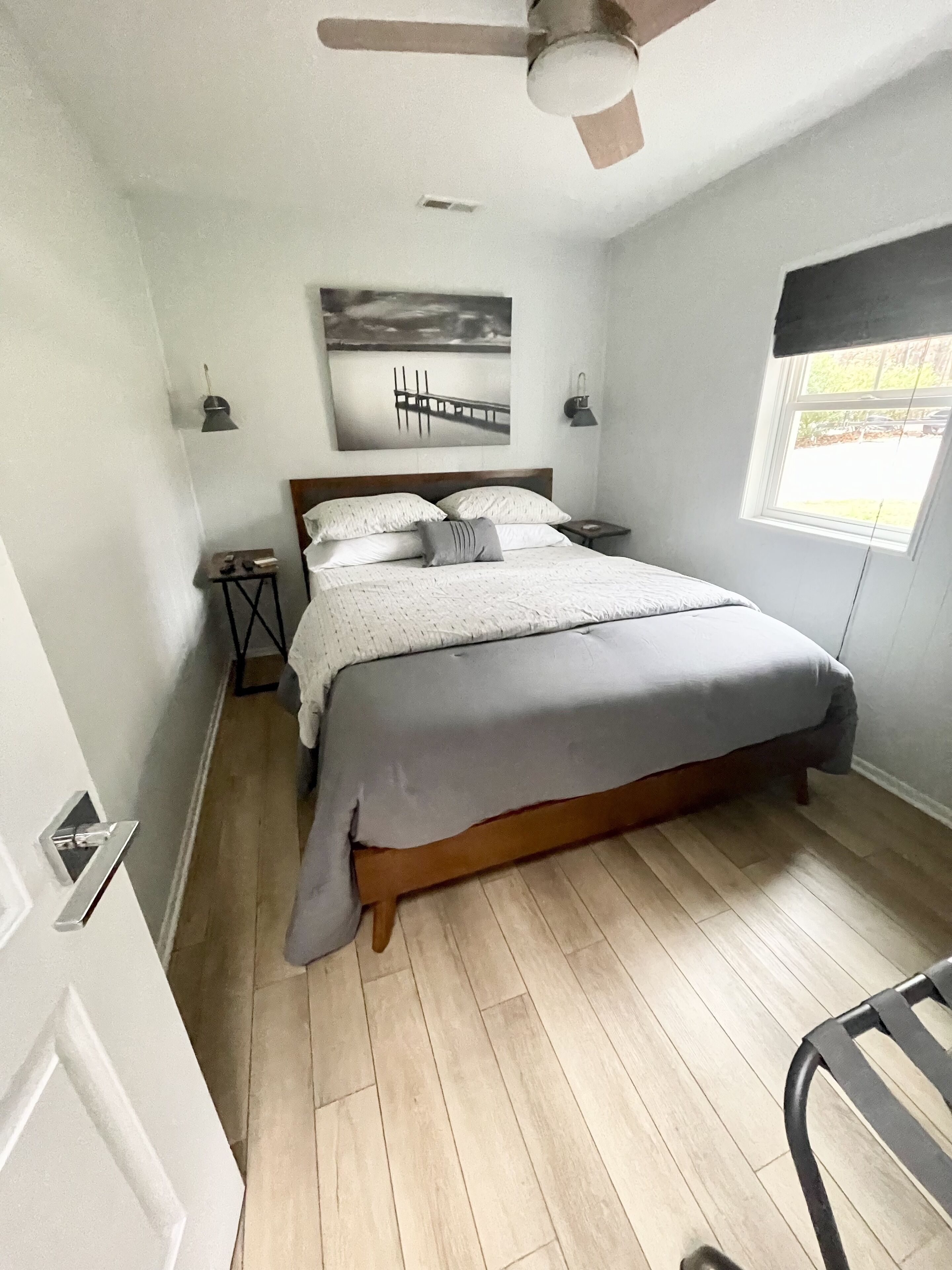 Een slaapkamer met een bed, een plafondventilator, een raam en een schilderij aan de muur.