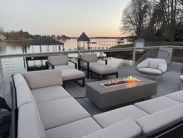 A deck with outdoor seating, a fire feature, and a view of a lake and dock.