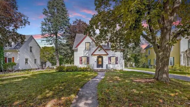 A two-story house with a stone foundation and a red roof, surrounded by a well-maintained lawn and trees. - The Arch House (Faribault)