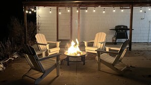 A covered outdoor seating area with a fire pit in the center, surrounded by Adirondack chairs. - The Arch House (Faribault)