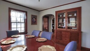 A dining room with a wooden table set for six, blue upholstered chairs, and a wooden cabinet with glass doors. - The Arch House (Faribault)
