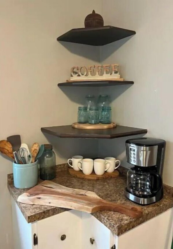A kitchen counter with a coffee maker, mugs, and a cutting board.