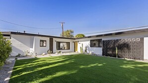A modern two-story house with a well-maintained lawn, a yellow door, and a decorative fence. - Private mini oasis steps from El Paseo! (Palm Desert)