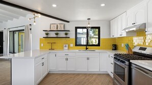 A modern kitchen with white cabinets, a yellow backsplash, and a large window. - Private mini oasis steps from El Paseo! (Palm Desert)
