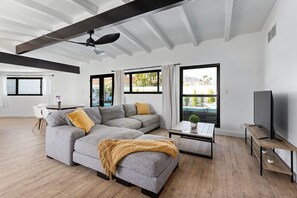 Una sala de estar moderna con un sofá modular, una mesa de centro, un televisor y ventanas amplias con cortinas.