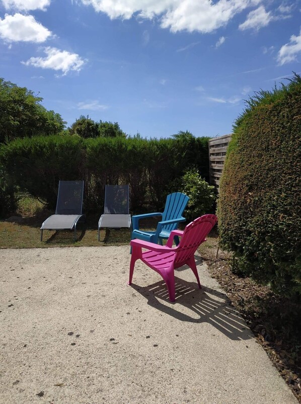 A patio area with outdoor seating including a pink chair, a blue chair, and a grey lounge chair.
