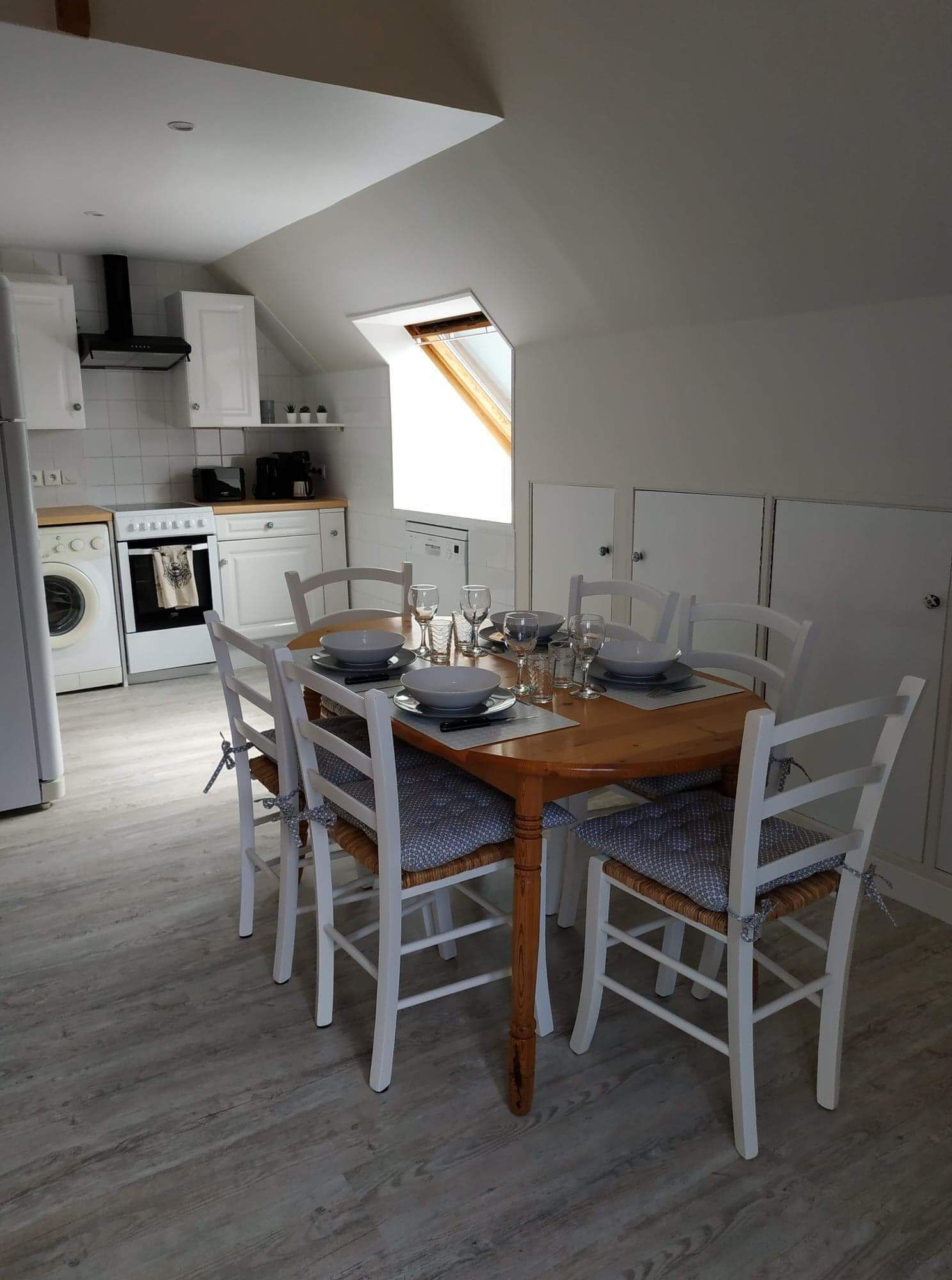 A modern kitchen with white cabinetry, a wooden dining table with white chairs, and a skylight above the table.