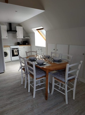 Una cocina moderna con armarios blancos, una mesa de comedor de madera con sillas blancas y un tragaluz sobre la mesa.