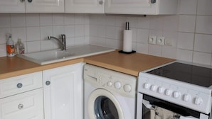A kitchen with white cabinets, a washing machine, an oven, and a sink. - "Le Gite tranquille" by the sea in Surtainville (Surtainville)