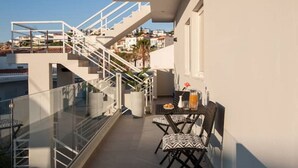 A balcony with a glass railing, a table with chairs, and a staircase leading to an upper floor. - Salty Colours Apartments in Almyrida (000)