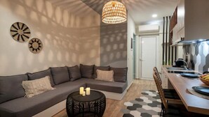 A modern living room with a gray sectional sofa, a round black side table, and a geometric-patterned rug. - Salty Colours Apartments in Almyrida (000)