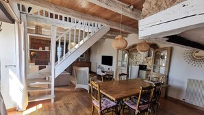 A rustic interior with a wooden staircase, a dining area with a wooden table and chairs, and a kitchen with stone walls and a fireplace. - The Gîte du Ligal in Najac (Najac)