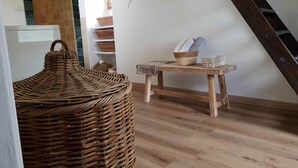 A room with a wooden floor, a wicker basket, a small table with a basket and towels, and a wall with a decorative branch. - The Gîte du Ligal in Najac (Najac)