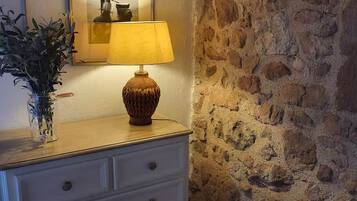 Une pièce avec un mur en pierre, une commode blanche à tiroirs, une lampe et un tableau encadré accroché au mur.