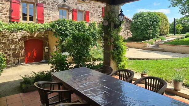 A stone building with red shutters and a covered patio area with a table and chairs. - The Gîte du Ligal in Najac (Najac)