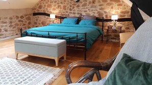 A cozy attic bedroom with a stone wall, a bed with blue bedding, two bedside tables with lamps, and a wooden bench. - The Gîte du Ligal in Najac (Najac)