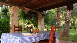 An outdoor patio with a checkered tablecloth, wooden chairs, and a bottle of wine.