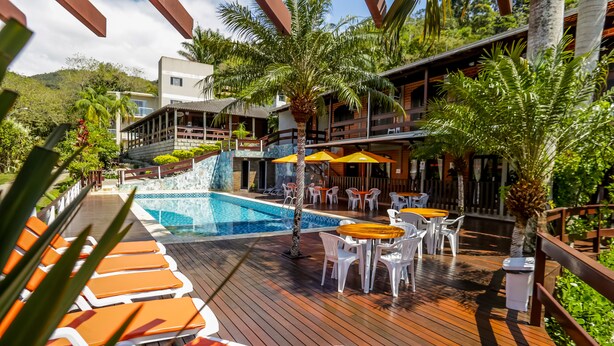 Zona de piscina en un resort, con terraza de madera, sillas de descanso y mesas con sombrillas.