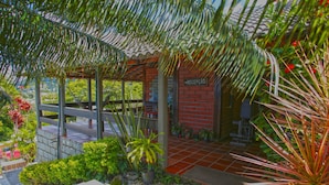 Un área de recepción con pared de ladrillo rojo, un letrero que dice "RECEPCAO" y una zona de estar al aire libre techada con suelo de baldosas.
