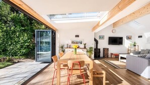 A modern interior with a wooden dining table, red chairs, a sofa, and a TV mounted on the wall. - Trevint - Modern beach house in Falmouth, private parking (Falmouth)