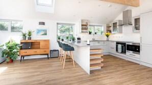 A modern kitchen with white cabinetry, a wooden island with bar stools, and a large window providing natural light. - Trevint - Modern beach house in Falmouth, private parking (Falmouth)