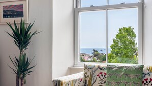 Habitación con vista a un pueblo costero, una planta en maceta y un sofá con un cojín estampado de cebra.