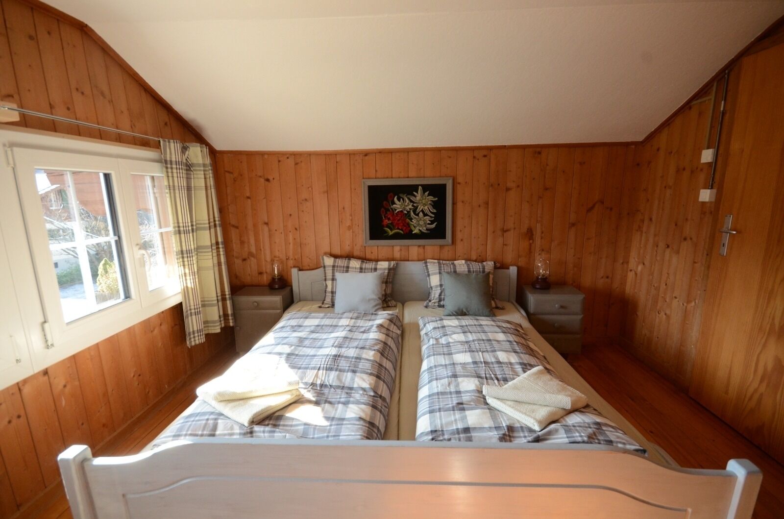 Un dormitorio con dos camas, paredes de madera, una ventana con cortinas y una obra de arte enmarcada en la pared.