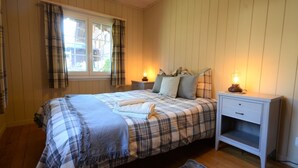 A bedroom with a plaid bedspread, two bedside lamps, a nightstand, and a window with curtains. - Traditional Chalet with views of the Eiger, Monch & Jungfrau! (Unterseen)
