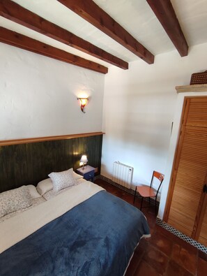 Une chambre à coucher comprenant un lit, une table de chevet, une lampe, une chaise, un radiateur et une armoire en bois.