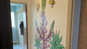 A hallway with a wall mural of flowers and bees, a door leading to another room, and a patterned rug on the floor. - Quiet single-level fully furnished house (Bangor)