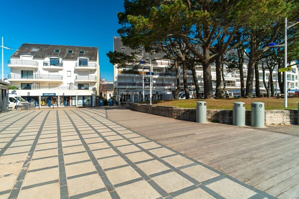 A paved walkway with a grid pattern, leading to a building with multiple balconies and a storefront.