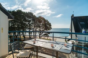 A balcony with a table and chairs overlooking a beach and the sea.