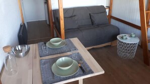 A bunk bed room with a grey sofa, a small dining table with plates and glasses, and a patterned rug. - Studio 2-3 pers. at the foot of the slopes (Mâcot-la-Plagne)