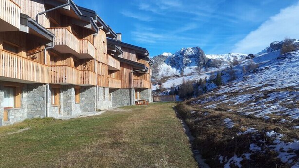 A wooden chalet with multiple balconies, stone walls, and a view of snow-capped mountains. - Studio 2-3 pers. at the foot of the slopes (Mâcot-la-Plagne)