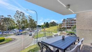 A balcony with a table and chairs, overlooking a busy street and residential buildings.