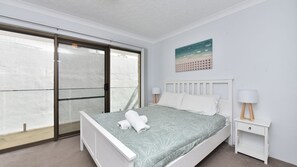 A bedroom with a bed, a nightstand, a lamp, a painting, and a sliding glass door.