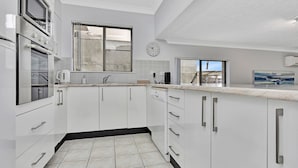 Una cocina moderna con armarios blancos, electrodomésticos de acero inoxidable, una ventana y un reloj en la pared.