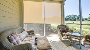 Un porche cubierto con muebles de mimbre, un banco acolchado y vistas a un campo de golf.