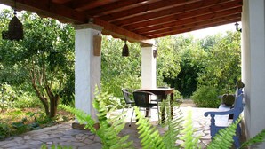 An outdoor patio with stone flooring, a wooden pergola, a table with chairs, and lush greenery. - Finca la Hijuela, Casa Azahar Andalucía; Cádiz; Vejer de la Frontera; (Vejer de la Frontera)