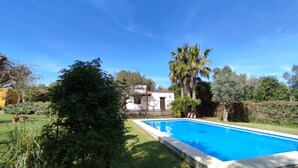 A rectangular swimming pool with a wooden deck, surrounded by lush greenery and a clear blue sky. - Finca la Hijuela, Casa Azahar Andalucía; Cádiz; Vejer de la Frontera; (Vejer de la Frontera)