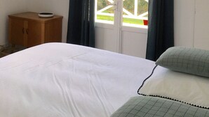 Ett sovrum med en säng, ett träskåp, en rund spegel och ett fönster med gardiner.