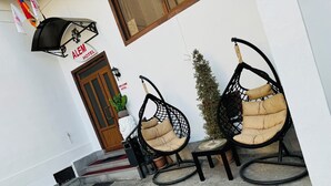 A hotel entrance with a wooden door, a welcome sign, and two black hanging chairs with cushions.