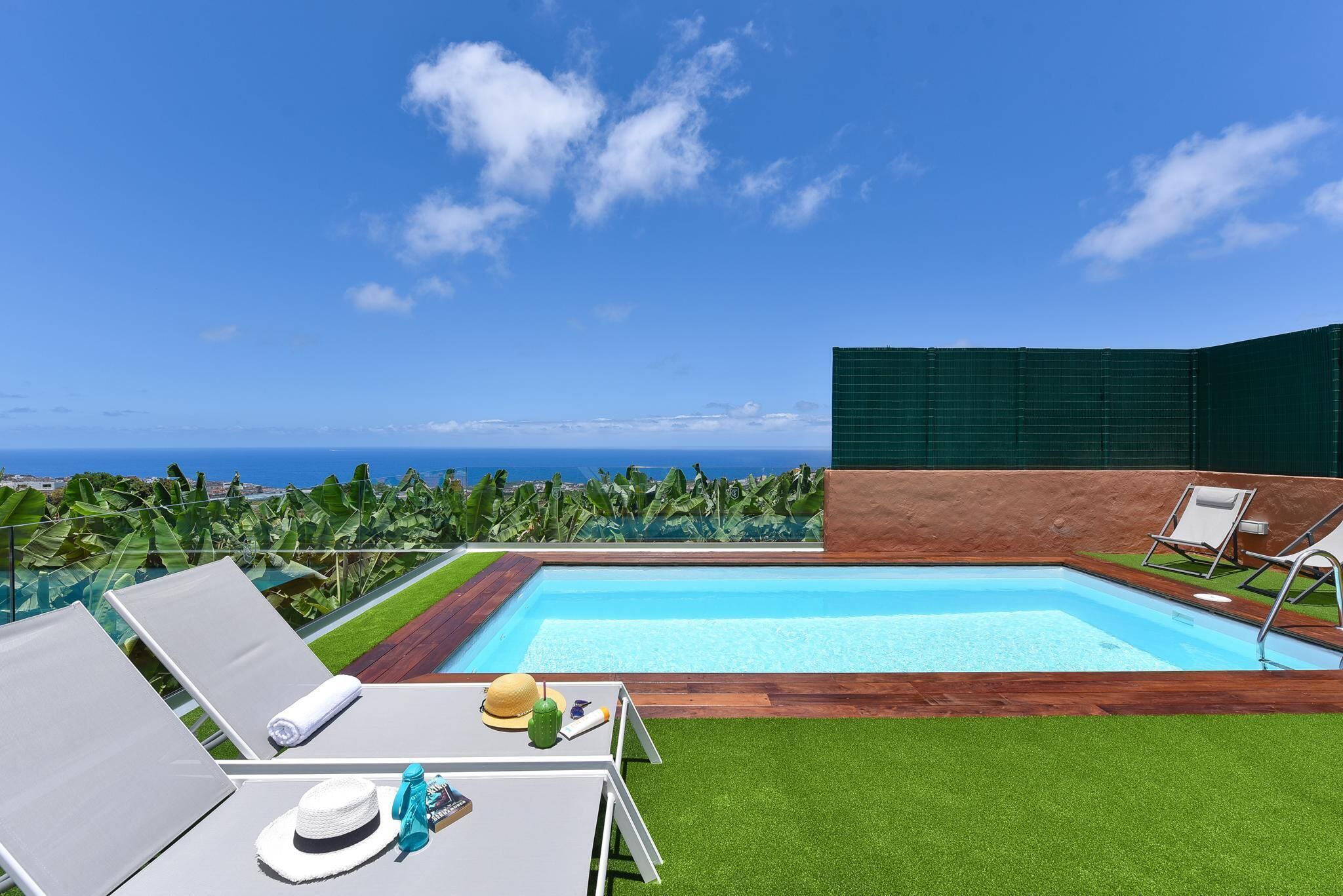 A rooftop pool with a clear view of the ocean, surrounded by lush greenery and modern architecture.
